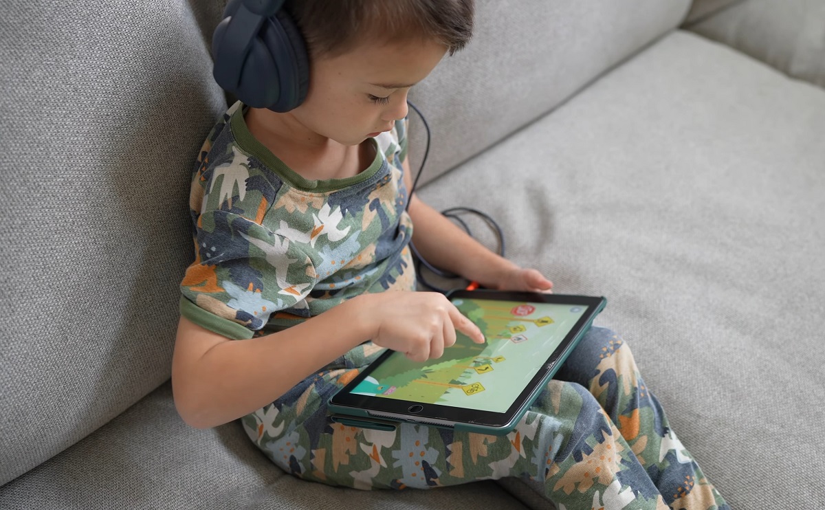 A young boy wearing headphones sits on a couch, engaging with an educational game on a tablet